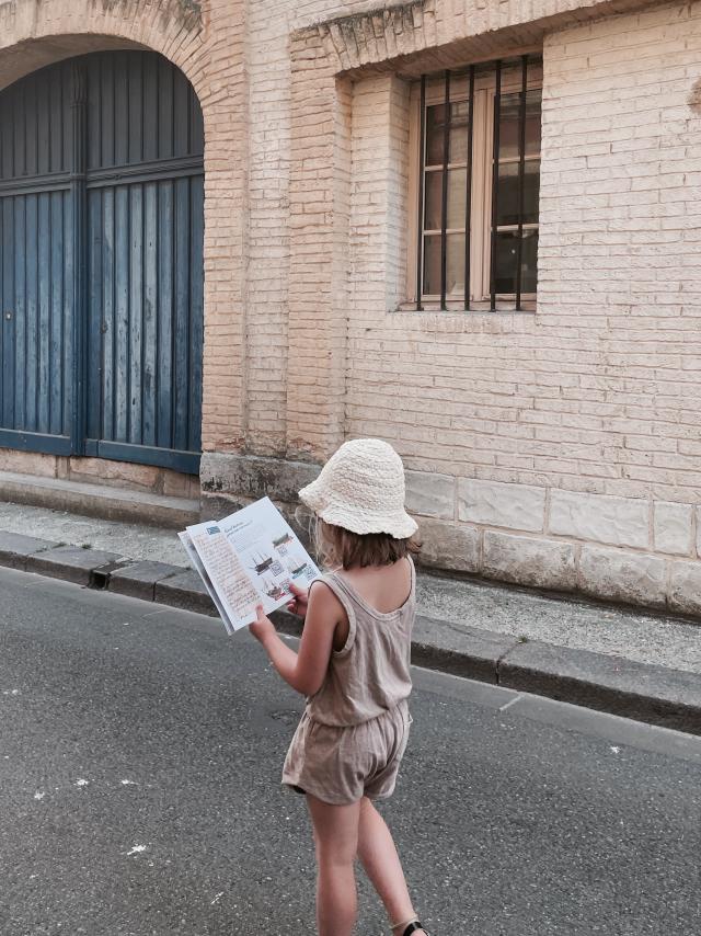 Une petite fille en tenue estivale lit son livret du jeu de piste 