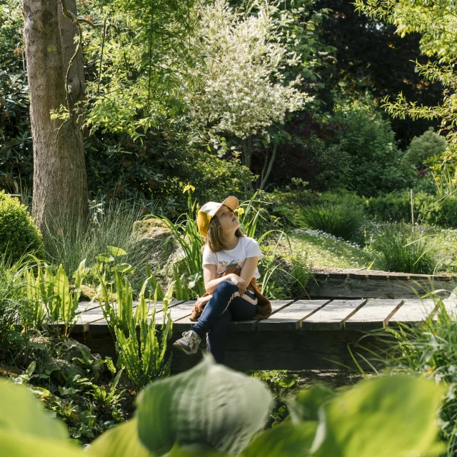 Une petite fille assise sur un pont au milieu d'un jardin verdoyant