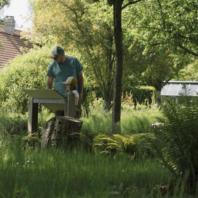 Un papa et sa fille consultent une table de lecture au coeur d'un jardin verdoyant