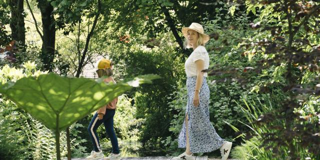 Une maman et sa fille en tenues estivales se baladent dans un jardin verdoyant à la végétation luxuriante