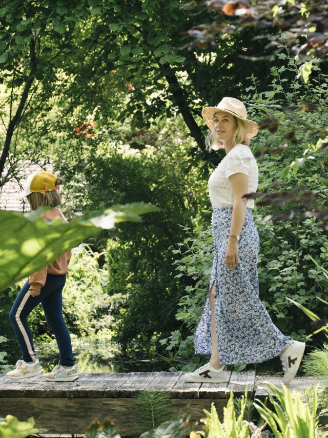 Une maman et sa fille en tenues estivales se baladent dans un jardin verdoyant à la végétation luxuriante