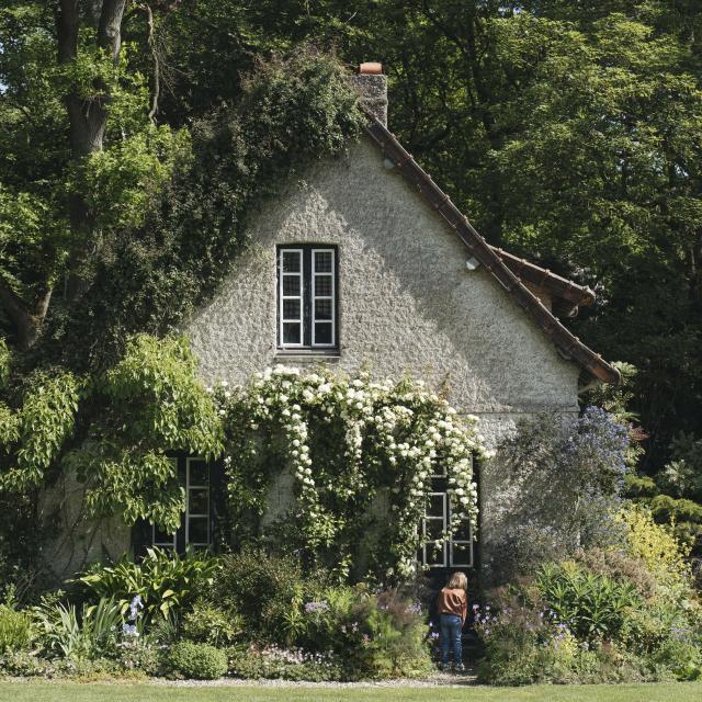 Une petite fille regarde à la porte d'une maison fleurie et bucolique au coeur d'un jardin verdoyant et arboré