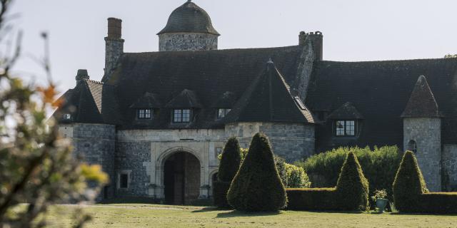 Un manoir de style renaissance en vieilles pierres avec une allée bordée de topiaires