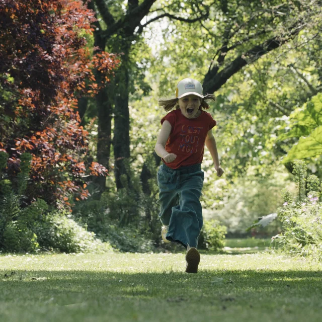 Une petite fille court en criant au coeur d'un jardin fleuri et arboré