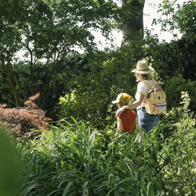 Une maman et sa fille se baladent dans un jardin arboré