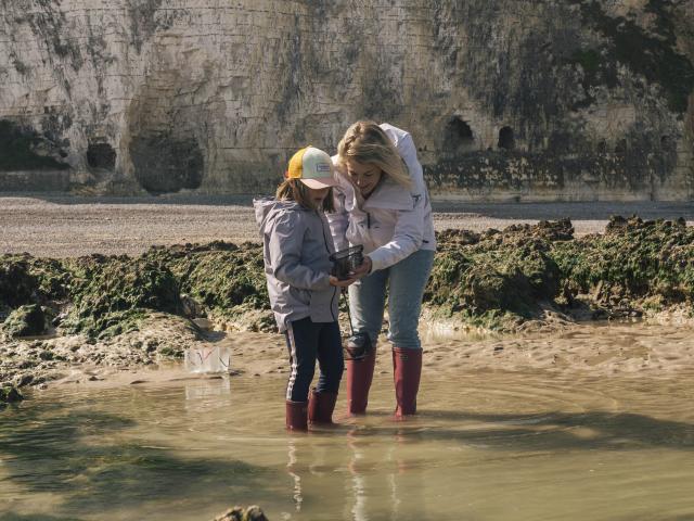 Une maman et sa fille en tenue de pêche à pied, observent quelque chose dans les mains de la petite fille , au milieu des rochers de la plage de Dieppe