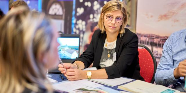 Une jeune femme de l'Office de Tourisme Dieppe-Normandie assise au stand d'un salon touristique