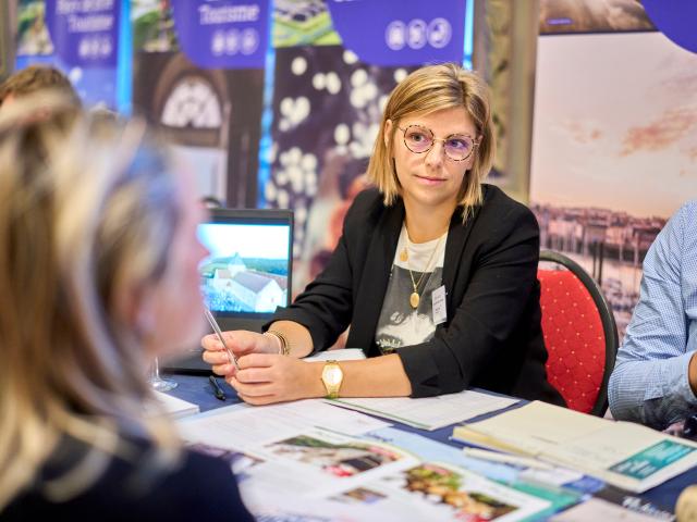 Une jeune femme de l'Office de Tourisme Dieppe-Normandie assise au stand d'un salon touristique