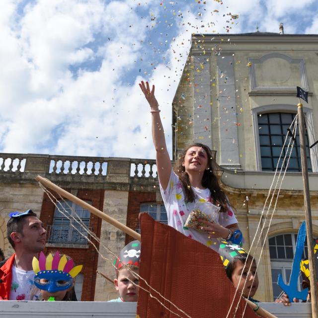 Une jeune femme accompagnée d'enfants à bord d'un char de carnaval lance des confettis