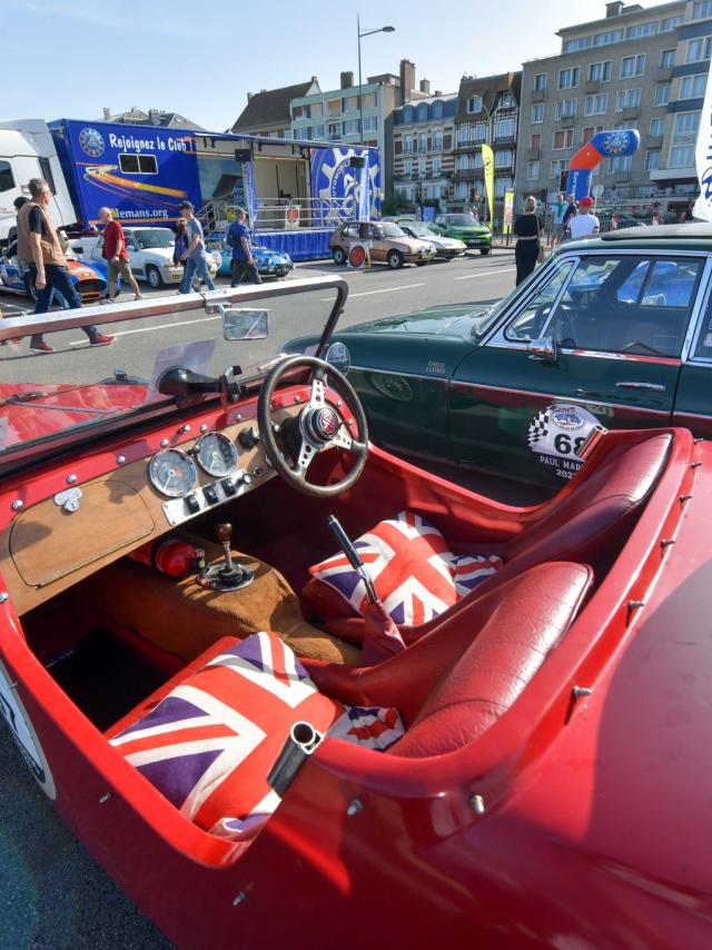 Une voiture décapotable rétro rouge aux sièges représentant le drapeau anglais exposée sur les pelouses de la plage de Dieppe avec d'autres véhicules anciens devant des passants