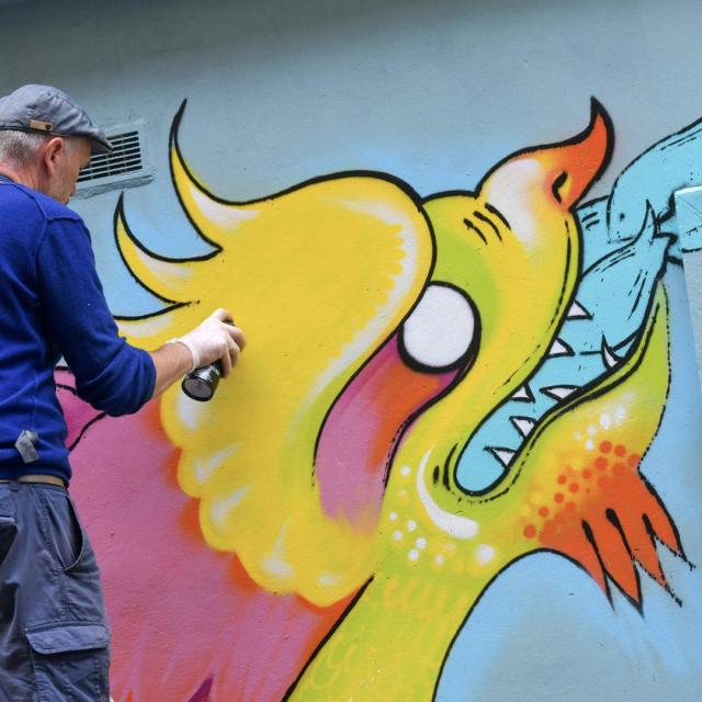 Un graffeur en train de peindre un dragon coloté sur un mur