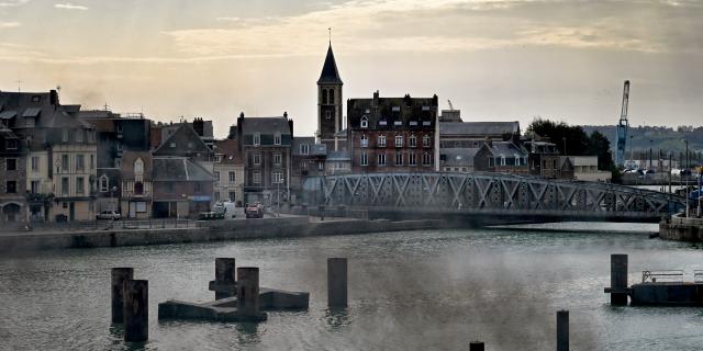 Le pont Colbert au-dessus de l'eau et le quartier du Pollet en arrière-plan, avec le clocher de l'église Notre-Dame des Grèves ; dans une lumière déclinante de fin de journée