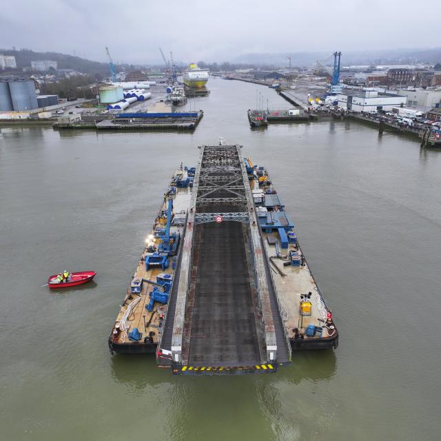 Un grand pont en fer de style Eiffel en travaux sur la barge qui le transporte dans le port.