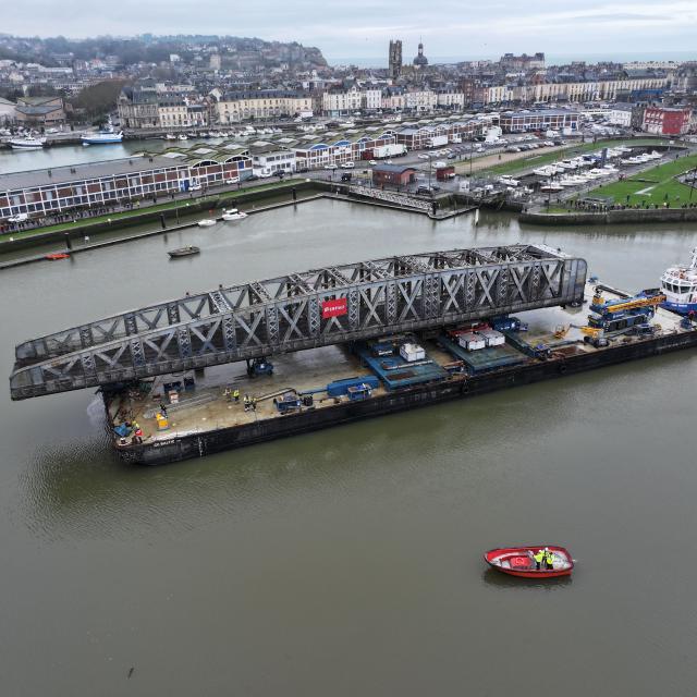 Un grand pont en fer de style Eiffel en travaux sur la barge qui le transporte dans le port.