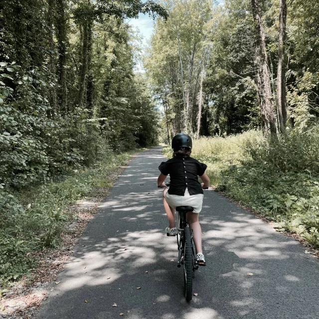 Jeune fille faisant du vélo sur l'Avenue Verte avec des arbres hauts de chaque côté de la route