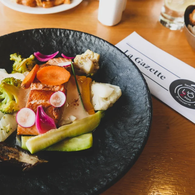 Plan rapproché d'une salade au poisson avec la gazette du restaurant l'O2 mer en fond