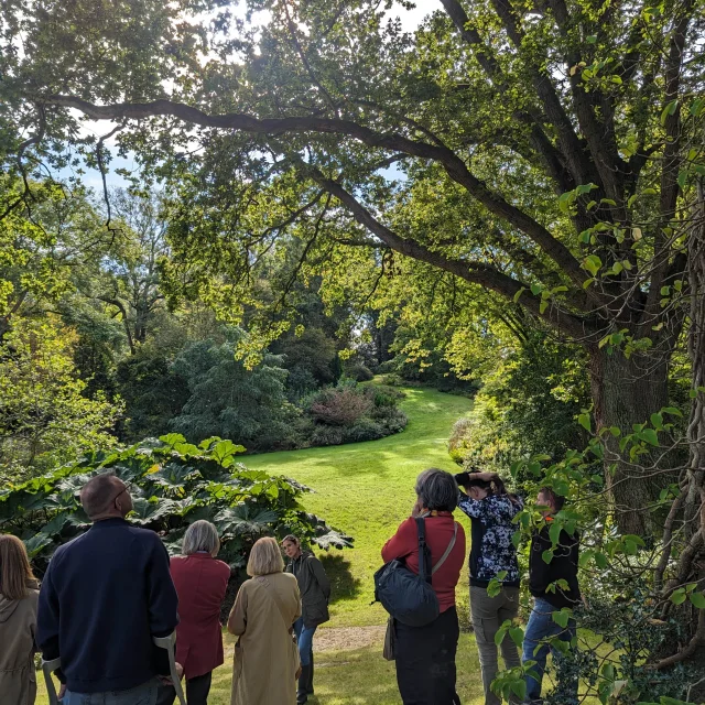 Groupe des personnes écoutant une guide conférencière dans un jardin fleuri