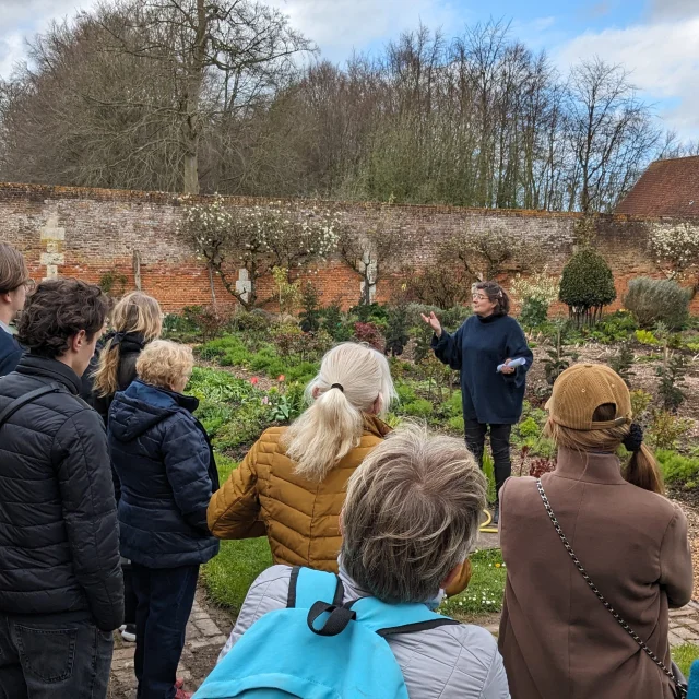 Guide conférencière dans un jardin donnant des explications à un public d'une quinzaine de personnes